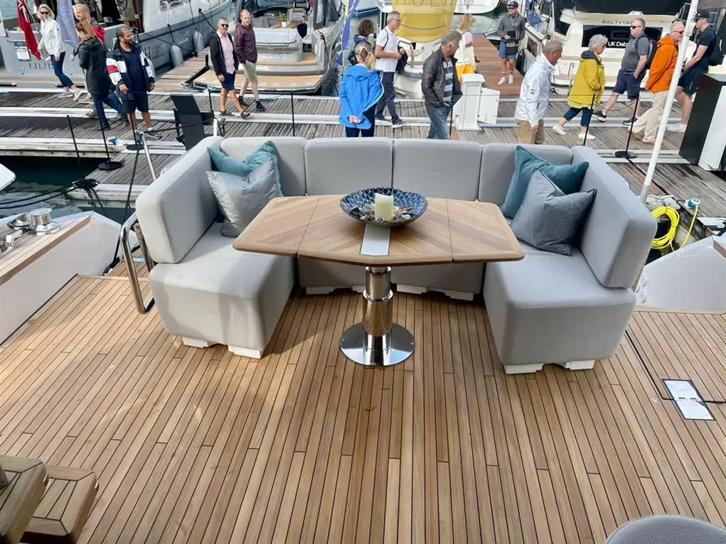 Luxury yacht deck featuring a stylish seating area with a table, surrounded by people in a bustling marina setting.